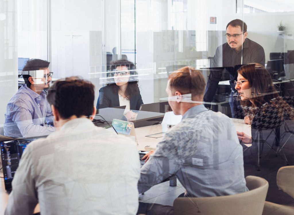 Team aziendale durante una riunione strategica in sala meeting con pareti in vetro.